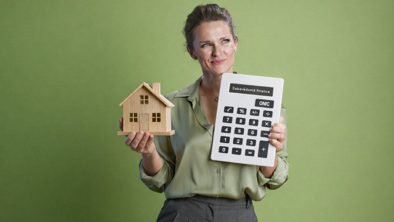 Ženy a investování – žena drží model domu a kalkulačku při plánování finanční strategie