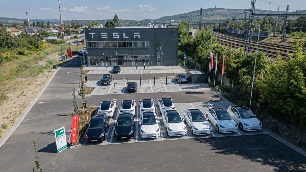 Flotila elektromobilů Tesla na venkovním parkovišti před budovou.