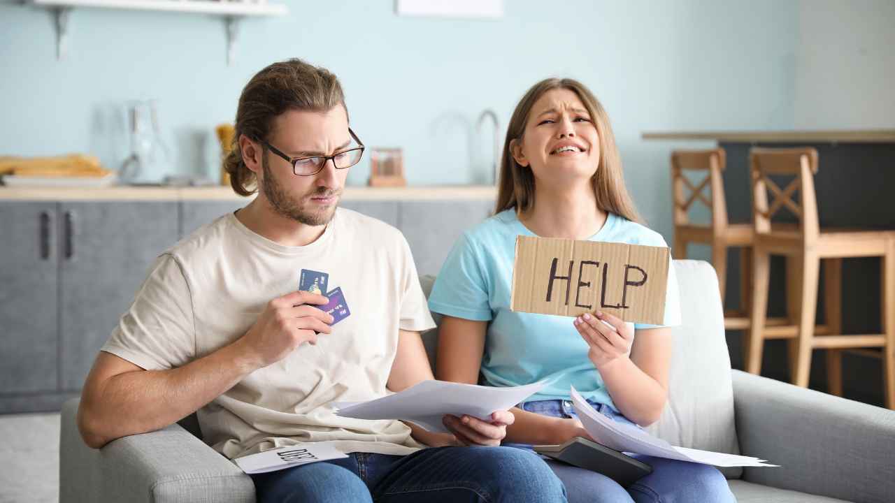 Peníze ve vztahu: muž počítá bankovky, zatímco žena drží cedulku s nápisem HELP.