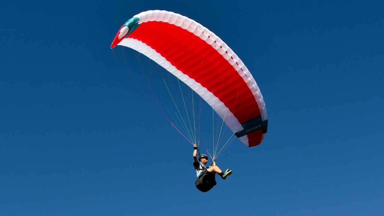 Paraglidista s červenobílým padákem na modré obloze při závodě Red Bull Dolomitenmann 2026.