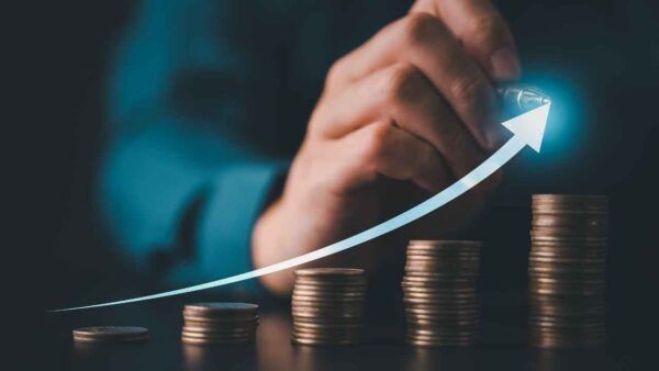 Ruka kreslí rostoucí šipku nad sloupci mincí jako ilustraci výnosu z investice.